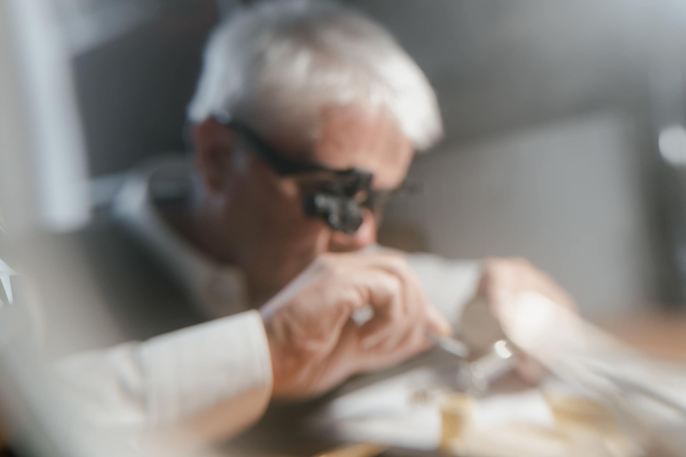 Un artisan penché sur son établi, loupe sur les yeux, travaille une pièce de précision.